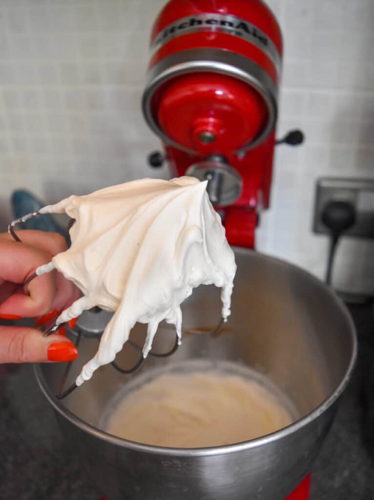 Close up of whisk from electric mixer showing stiff peaks of stable whipped cream.