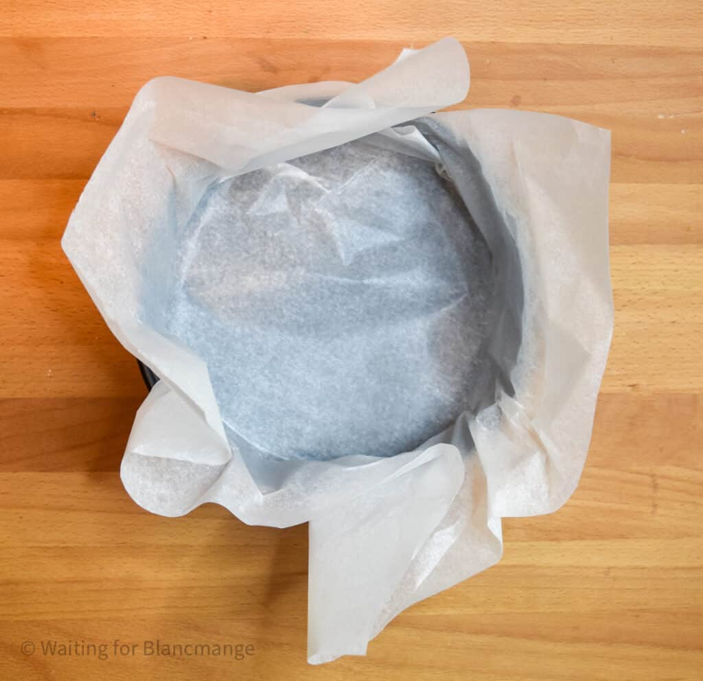 Spingform pan lined with overhanging parchment paper.