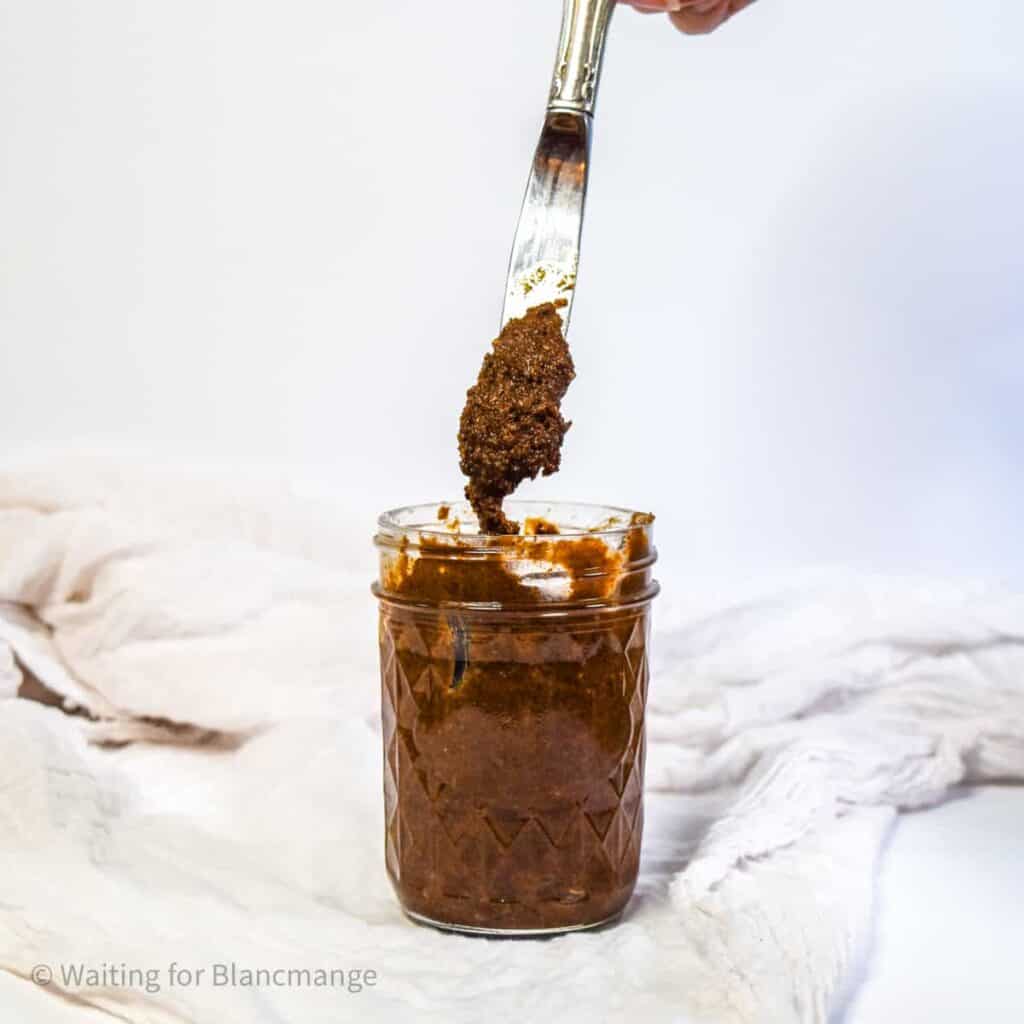 A knife being pulled out of a jar of candied pecan nut butter, showing the pecan paste.