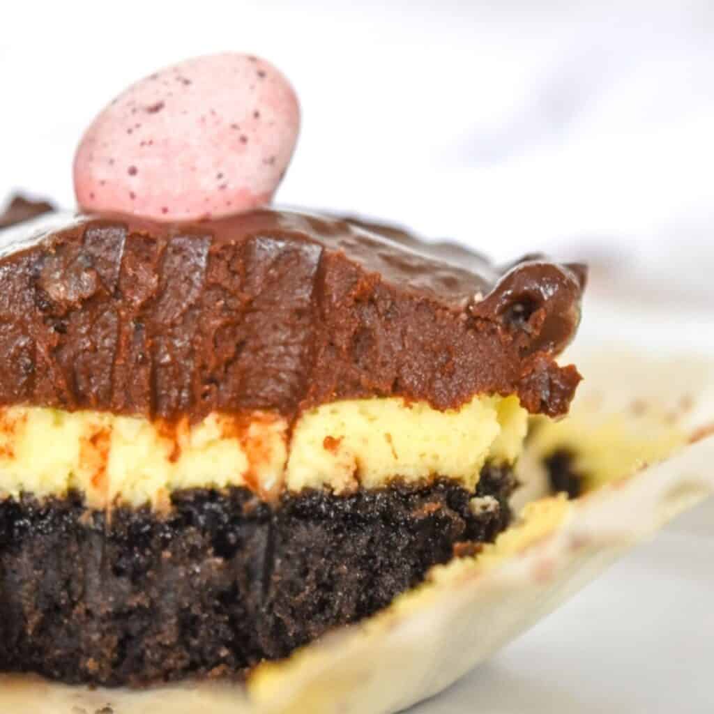 Close up of mini cheesecake with chocolate ganache sitting in its open cupcake wrapper after a bite has been taken.