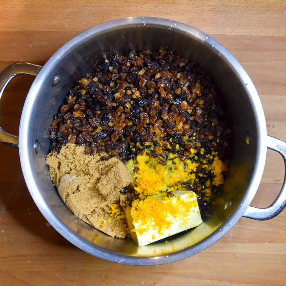 Overhead shot of a large deep pot filled with dried fruit, brown sugar, fruit juice, zest and butter.