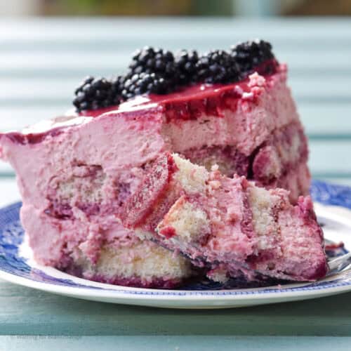 Close up shot of a slice of blackberry tiramisu. A fork has taken a bite out of the tiramisu which is sat on a small plate.