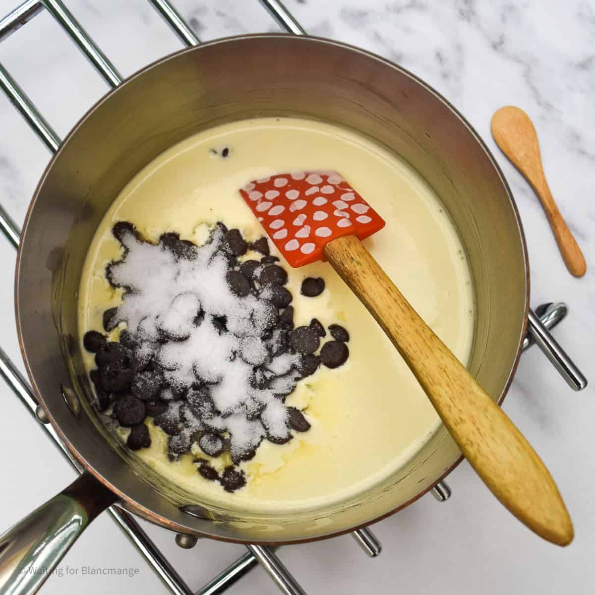 Overhead photo of saucepan with simmered vanilla cream, chocolate chips and sugar. There is a small spatula in the pan waiting to stir together.
