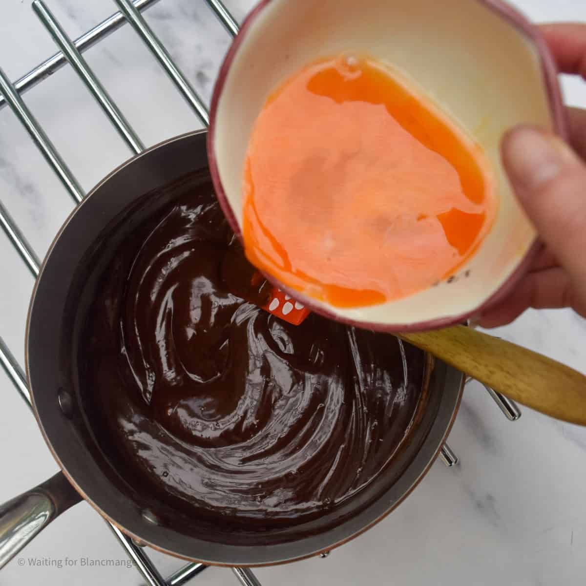 Overhead shot of adding lightly beaten egg into chocolate mixture in a saucepan.