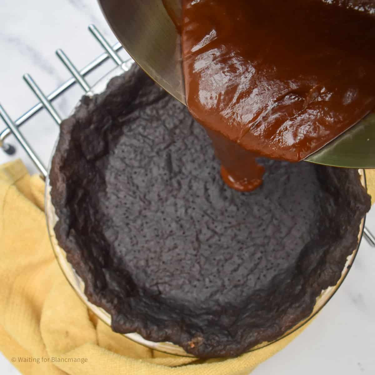 Overhead shot of pouring chocolate tart filling onto the base of a blind baked chocolate pastry shell in the background.